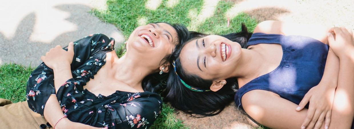 DirectAsia Insurance_Two females lying under a tree shade, smiling brightly on a sunny day