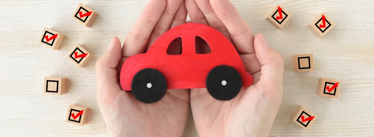 DirectAsia Insurance_Person holding a red car with several wooden checkbox cubes by the sides