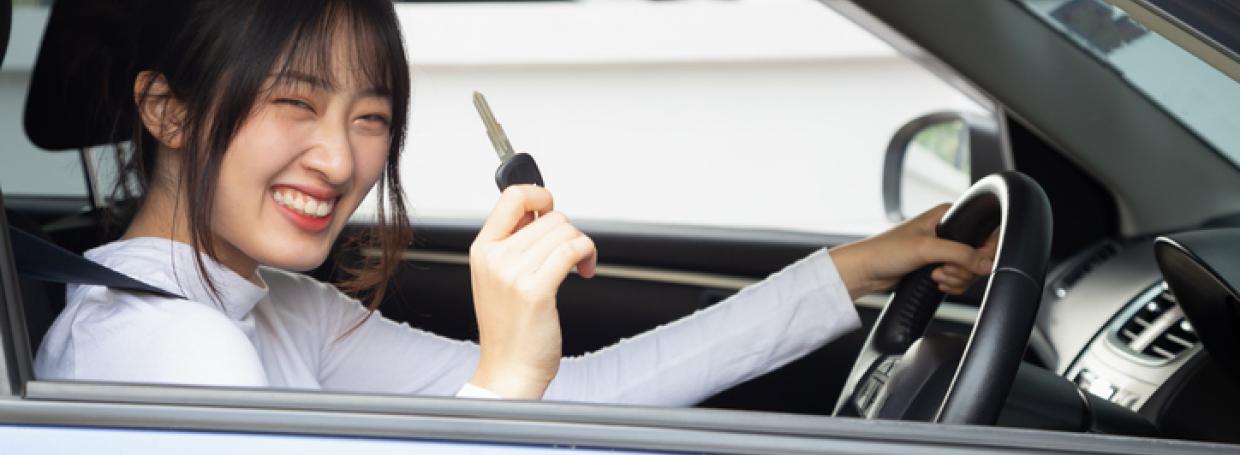 Young happy Asian car driver woman smiling and showing new car keys. Novice drivers concept